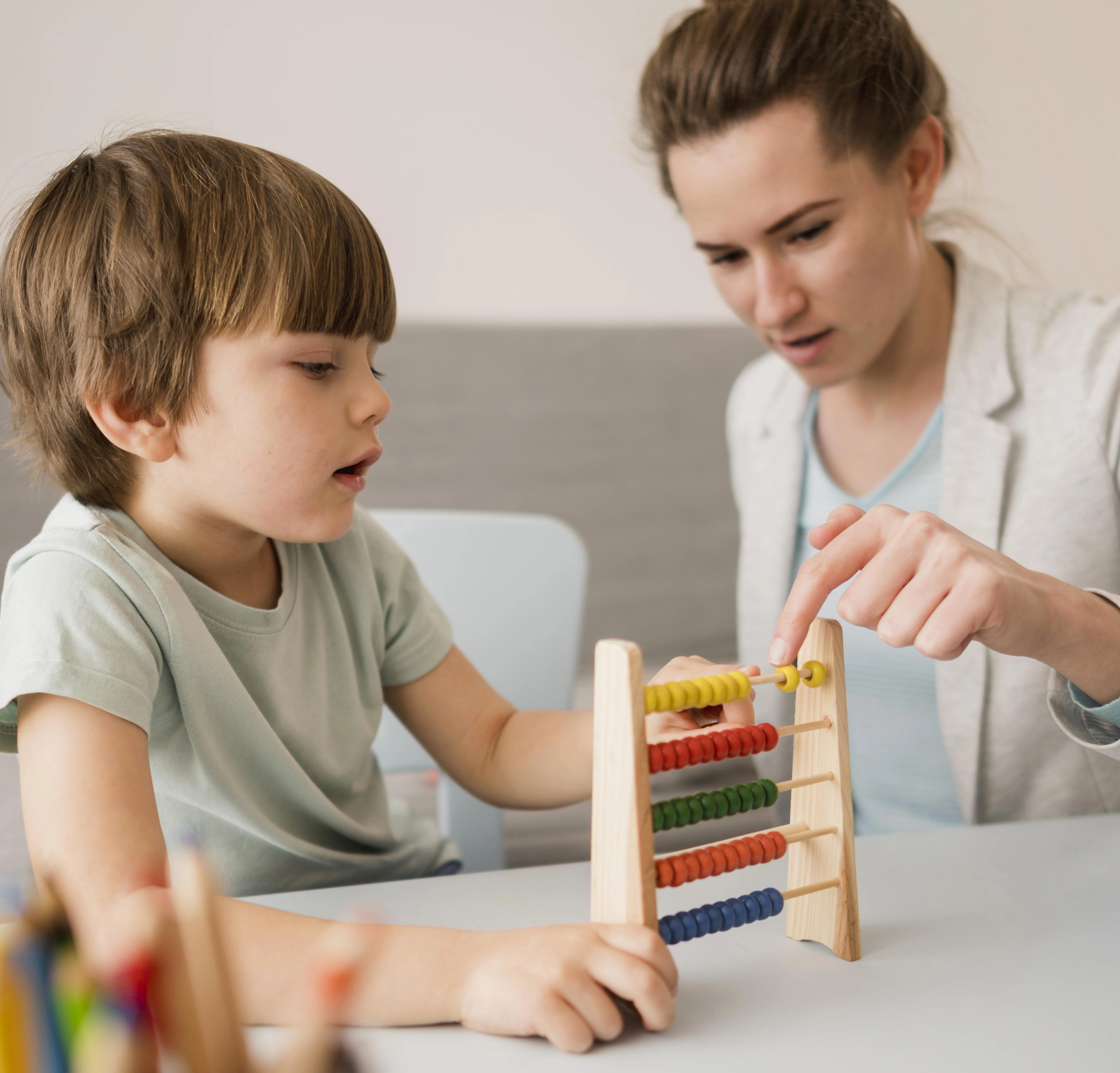 A therapist and a young boy use a colorful wooden abacus together during a therapy session.
