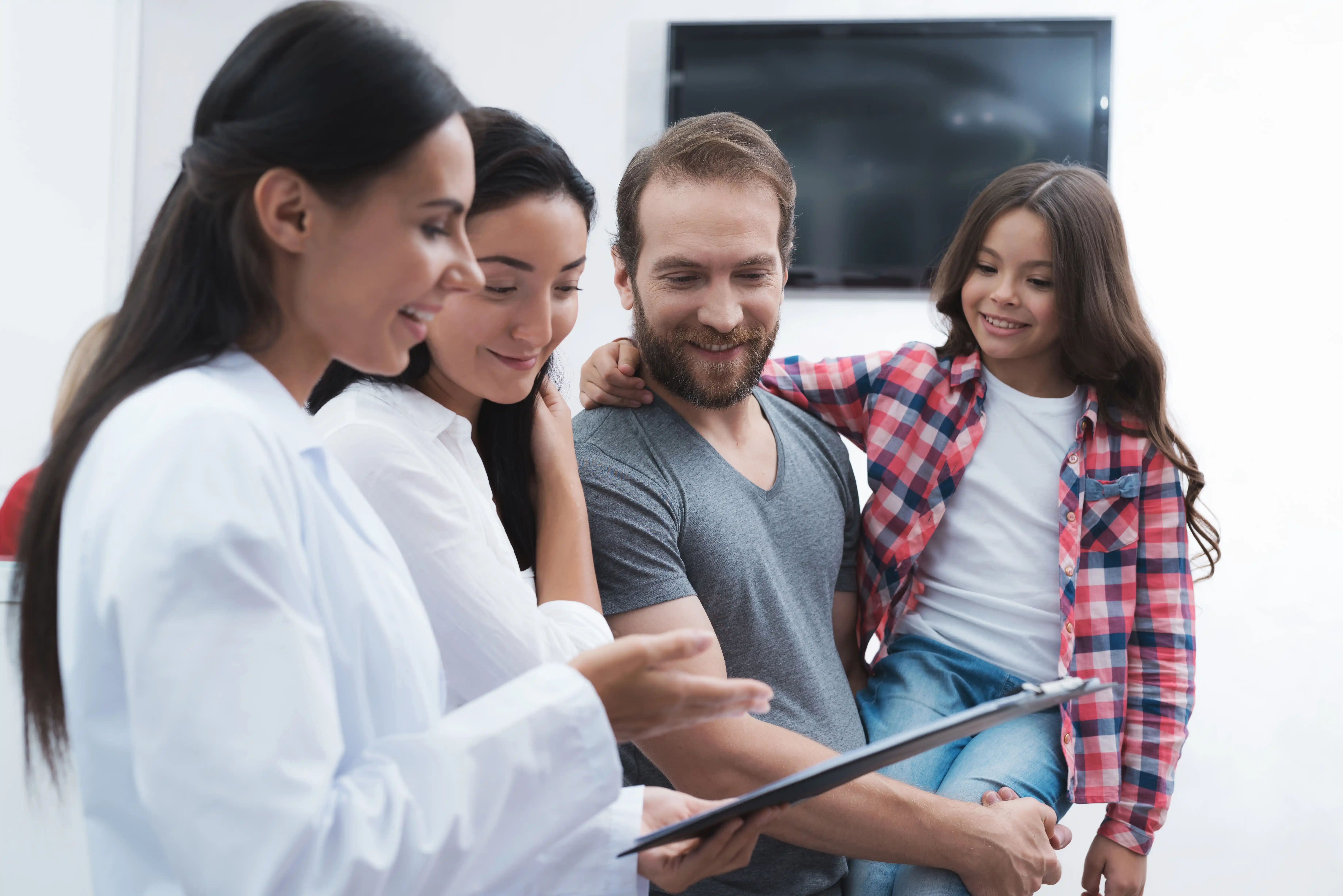 A clinician showing a tablet to a father and daughter, reviewing therapy progress together.